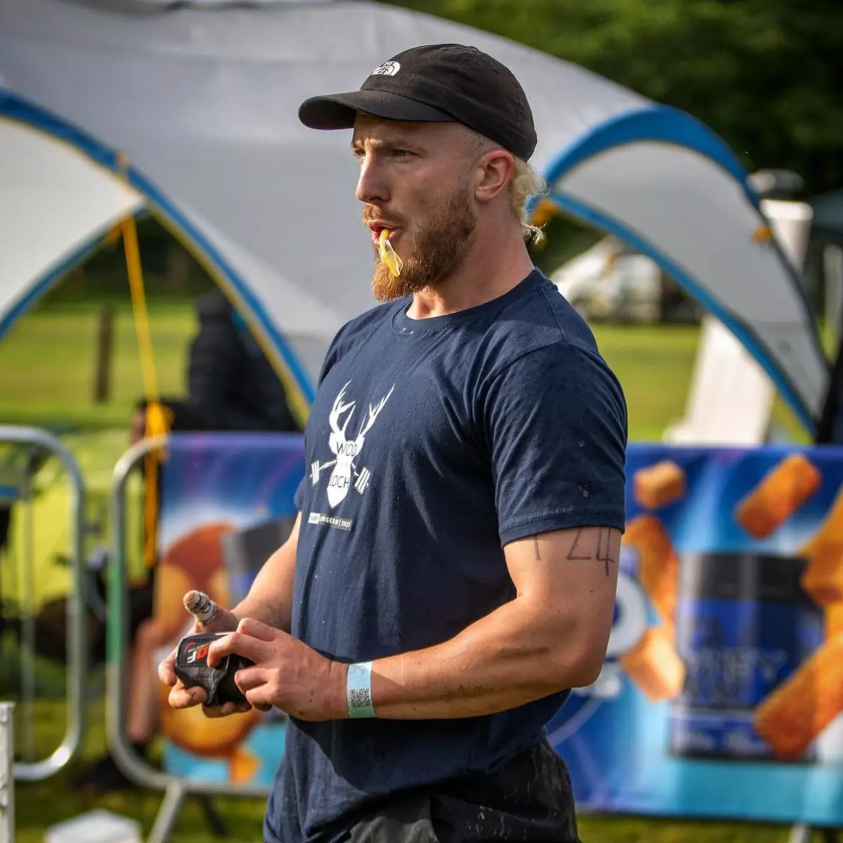 A man in a black cap and navy t-shirt stands outside eating a yellow snack.
