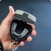 A hand holds an open black case with a clear mouthguard inside.