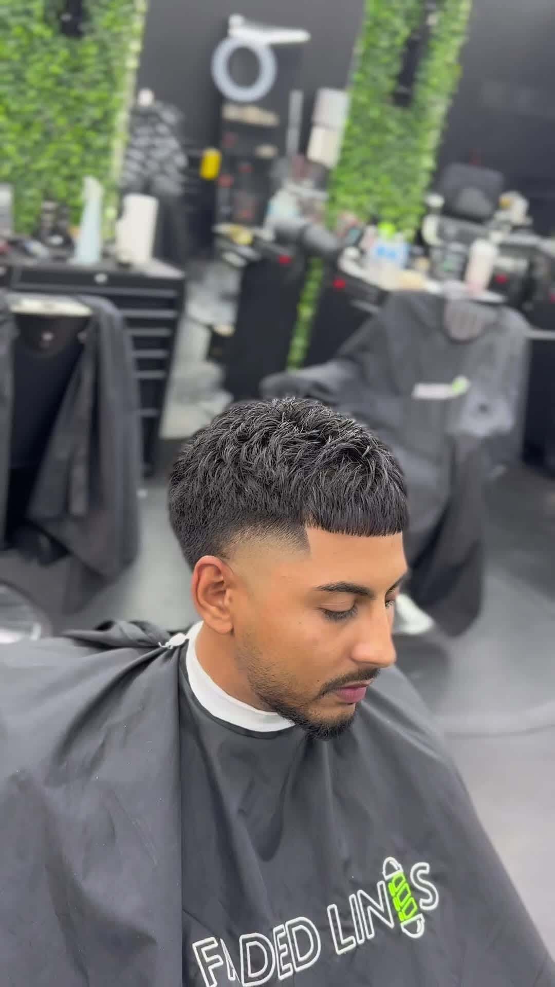 Man with a fresh haircut in a barbershop, wearing a black cape.