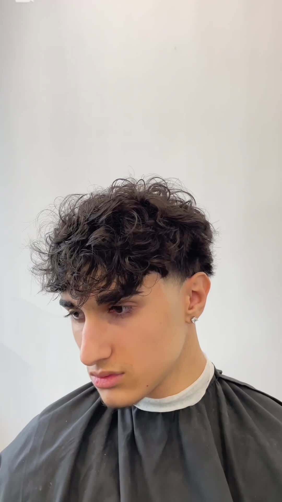 Person with curly hair and earrings in a barber's cape.