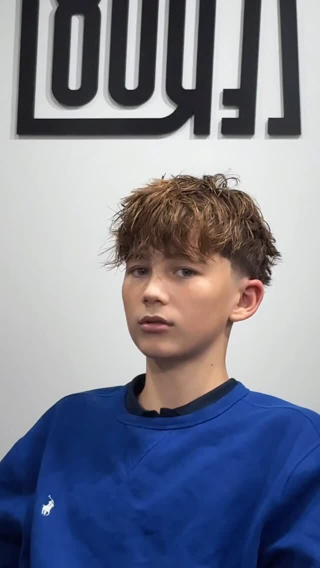 Young person with short hair wearing a blue sweatshirt, sitting indoors.
