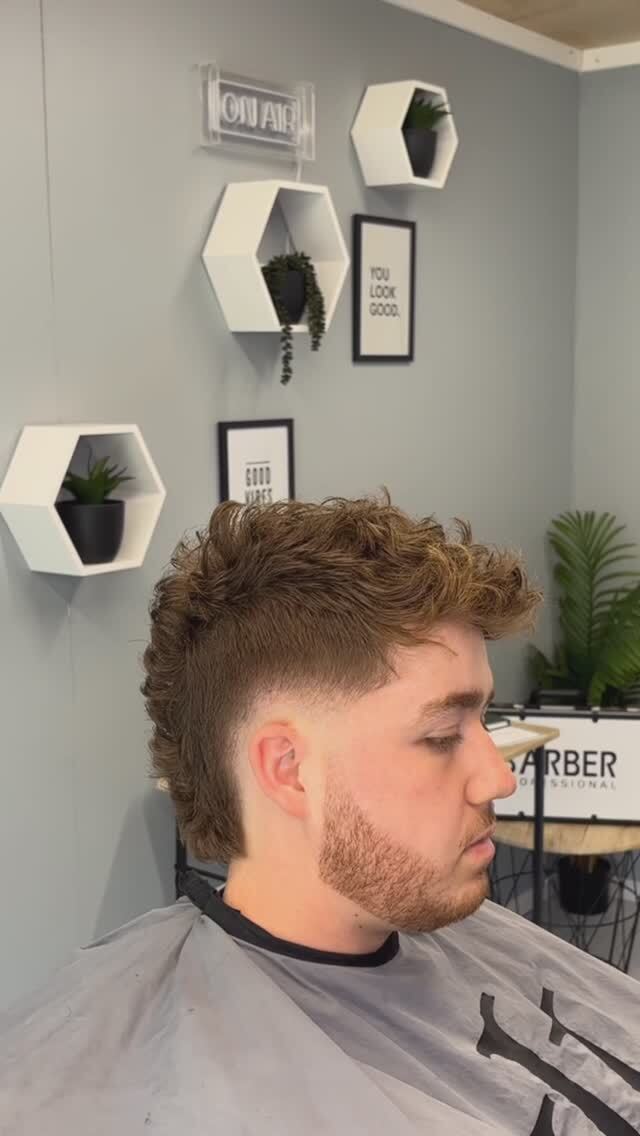 Man with a styled haircut in a barbershop, wall decor in background.