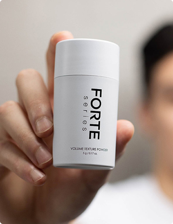 Hand holding a white bottle labeled 'FORTE series' volume texture powder.