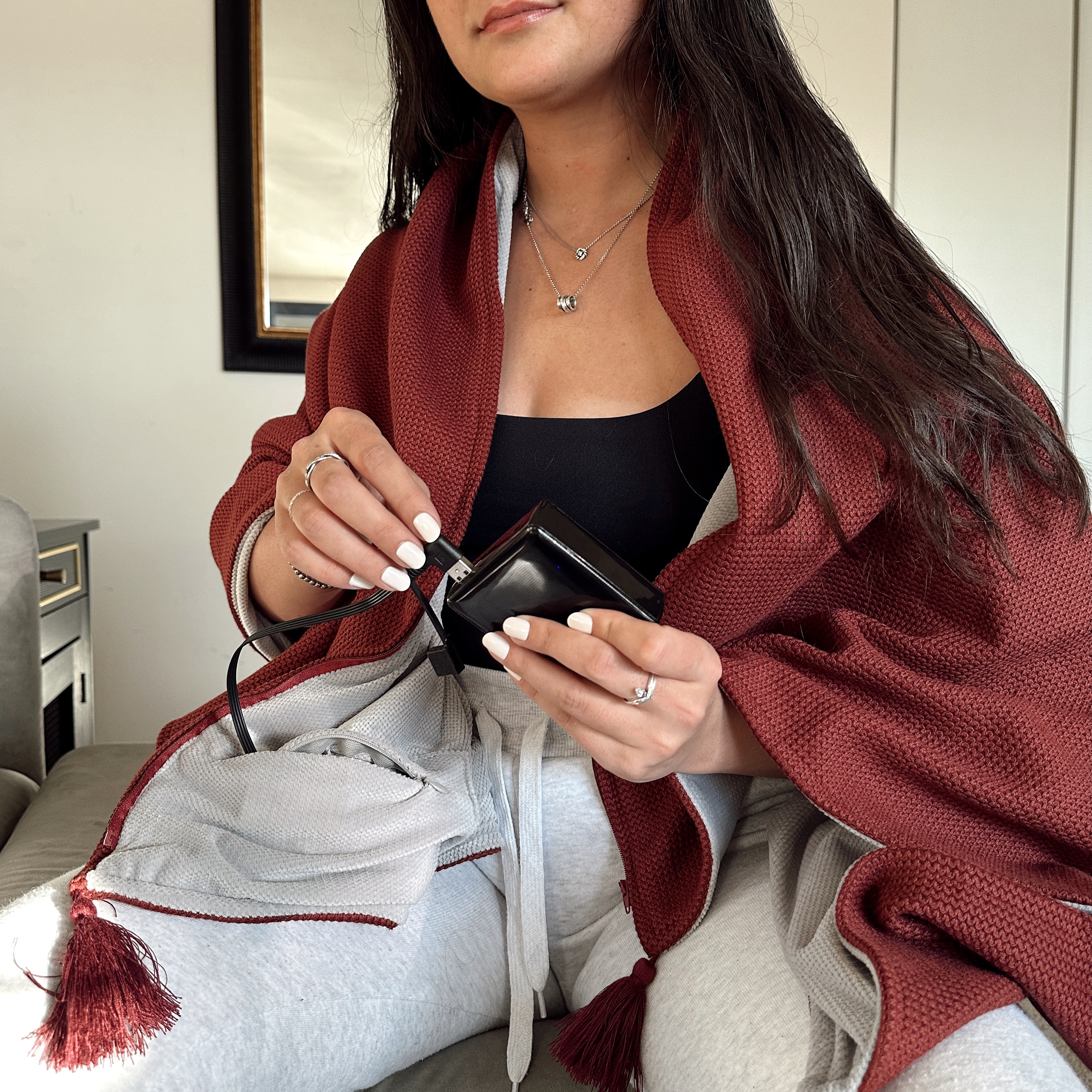Woman holding a small black device, wearing a red shawl, sitting on a couch.