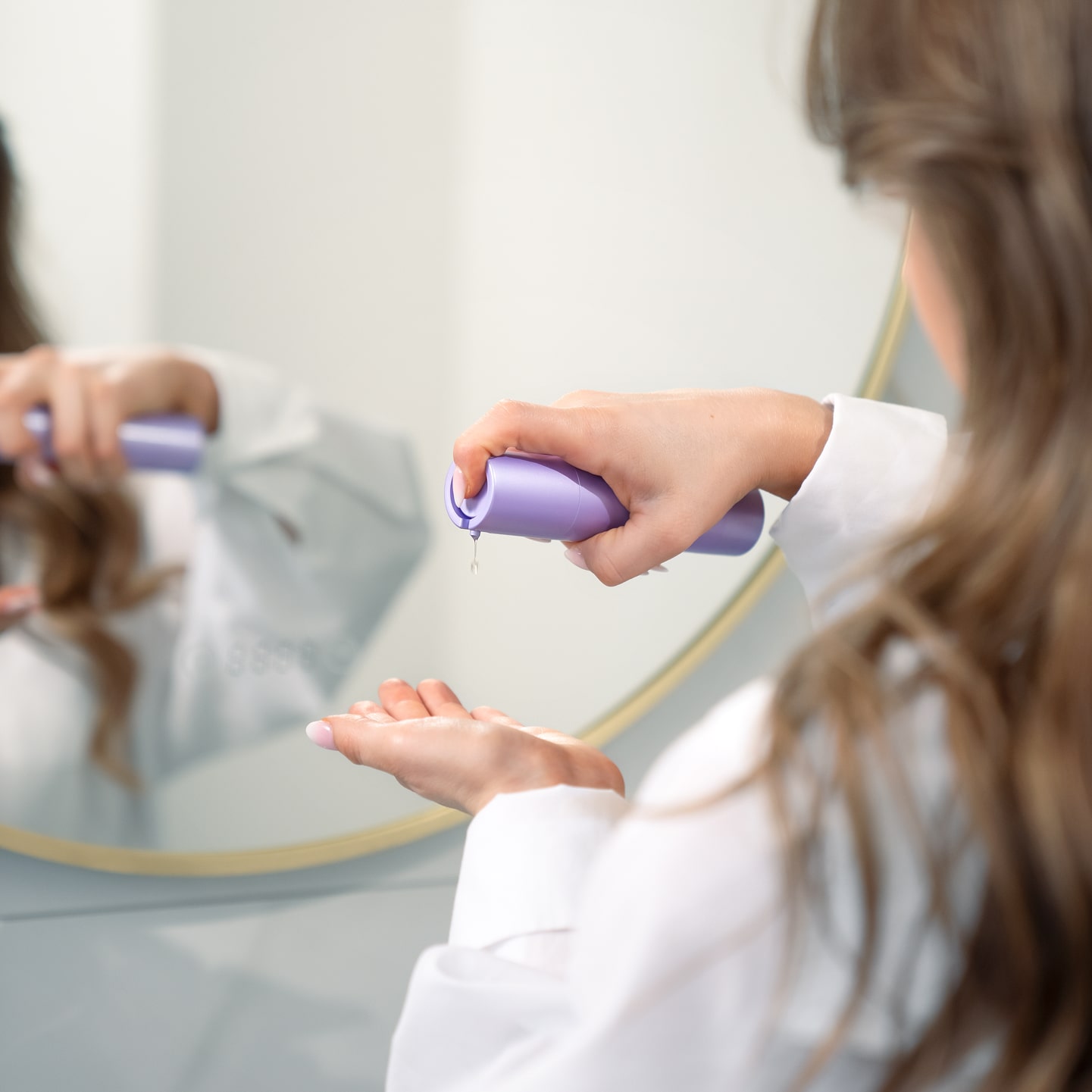 Person dispensing lotion from a purple bottle into their hand in front of a mirror.