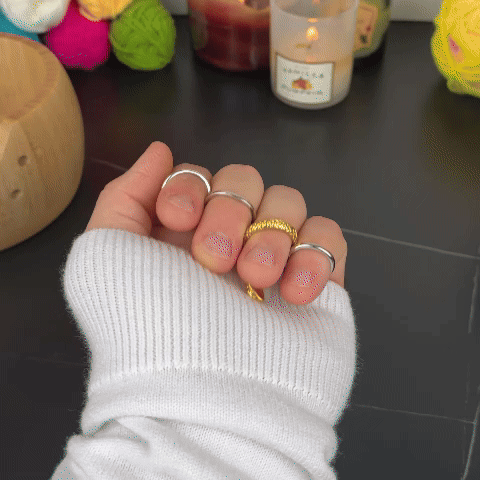 Hand with rings holding yellow yarn, surrounded by colorful yarn balls and a lit candle.