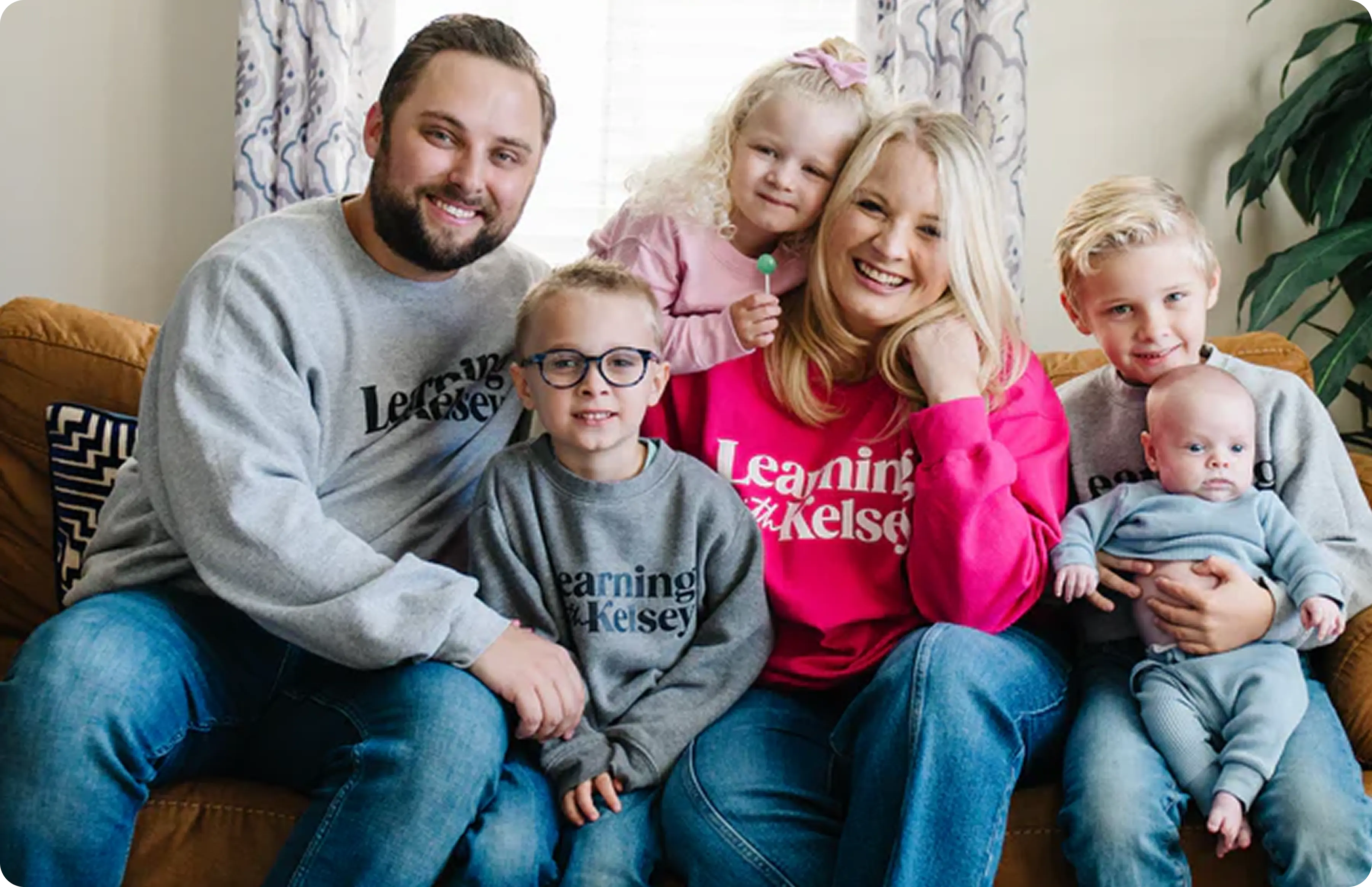 A family of two adults and four children sitting on a couch and smiling for a photo.