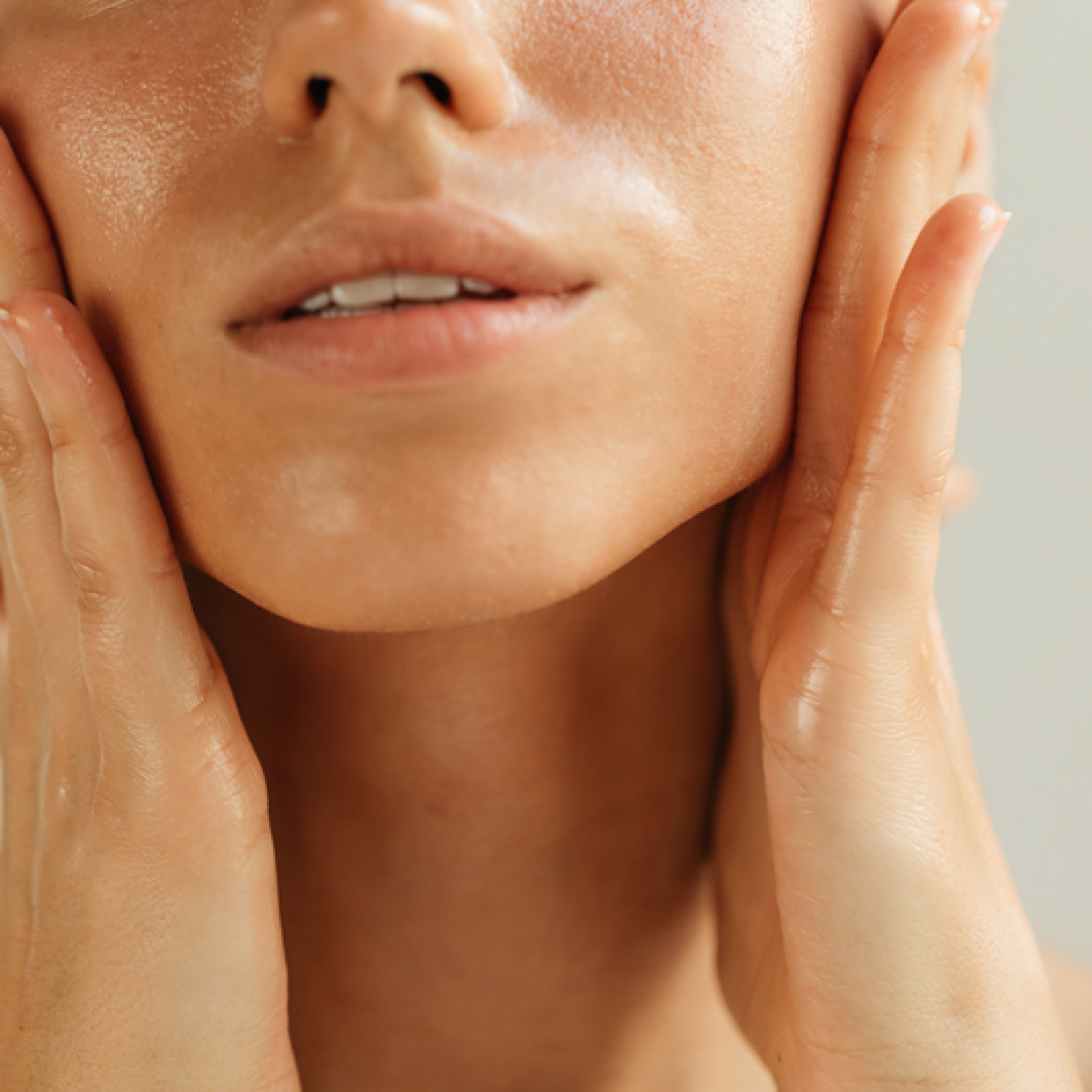 A close-up of a person with dewy skin cupping their face with their hands.