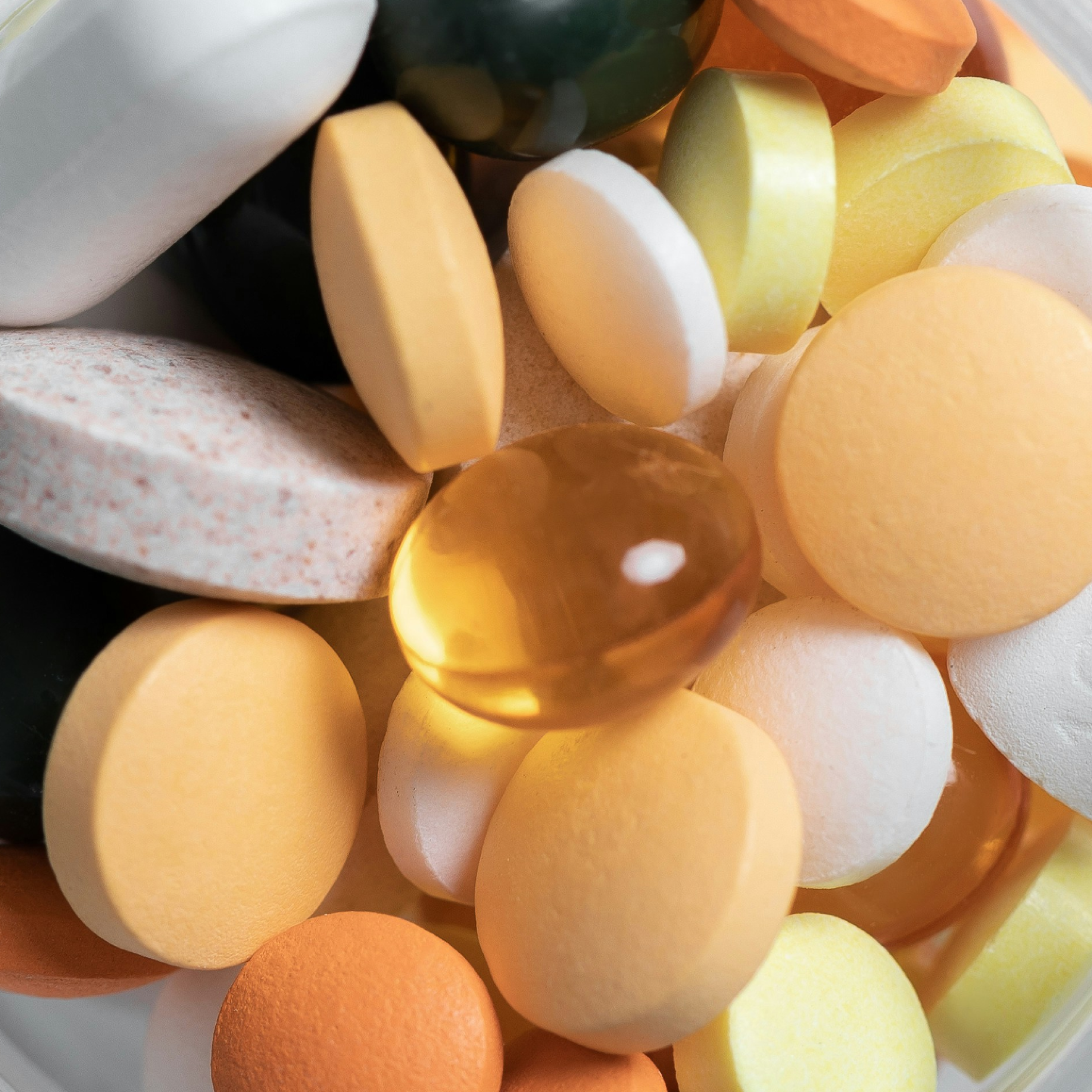 A close-up of assorted multi-colored pills, tablets, and gel caps in a pile.