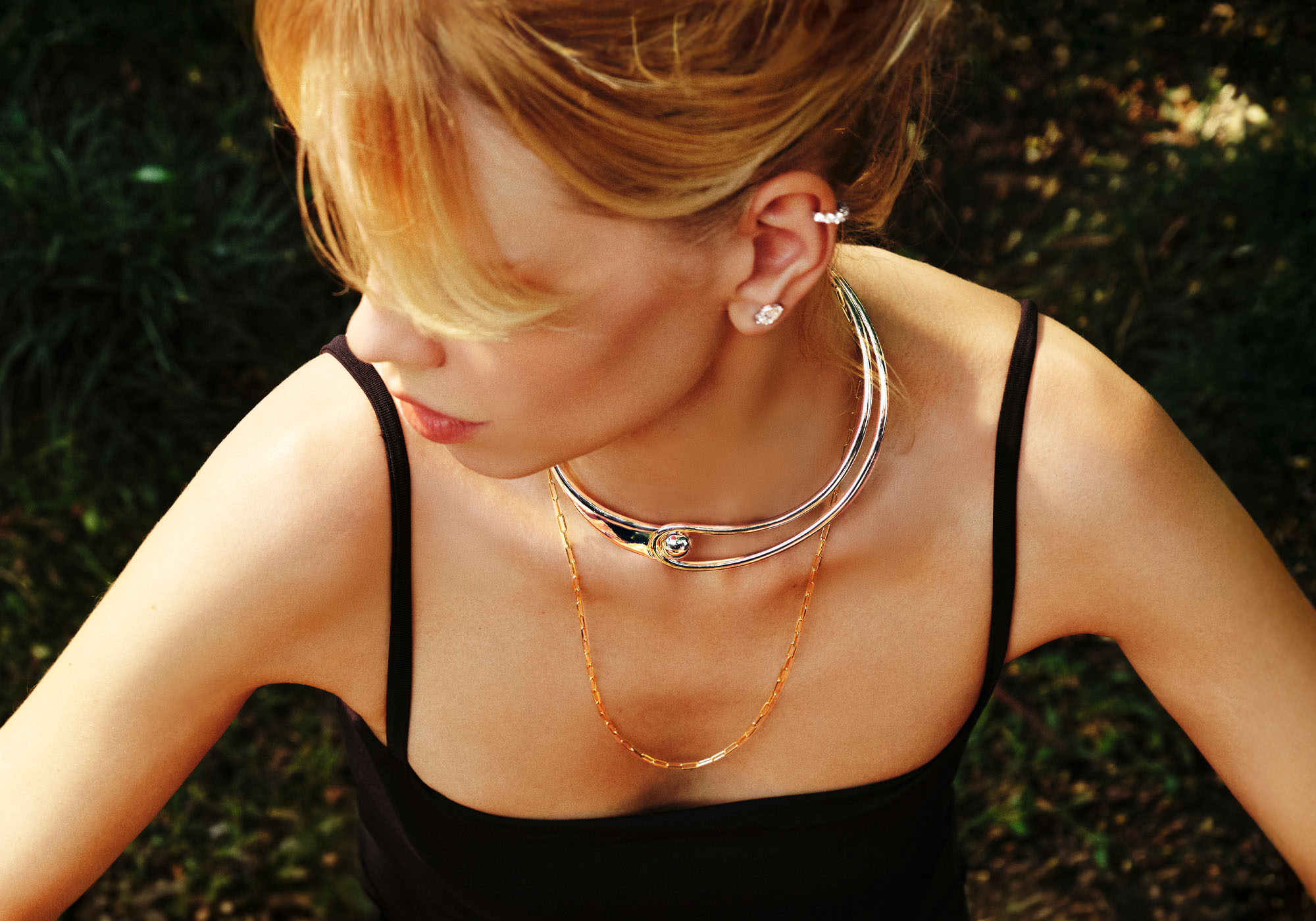 A high-angle view of a blonde woman wearing a silver choker, a gold necklace, and earrings.