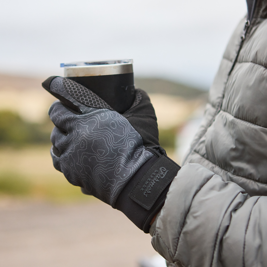 A person in a puffy jacket and patterned gloves holds a metal travel mug.