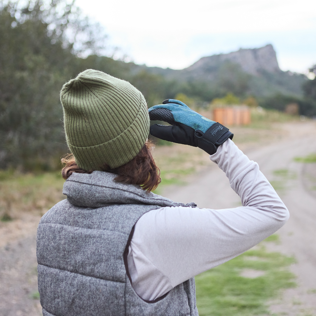 A person from behind wearing a green beanie and a glove looks out at a mountain.