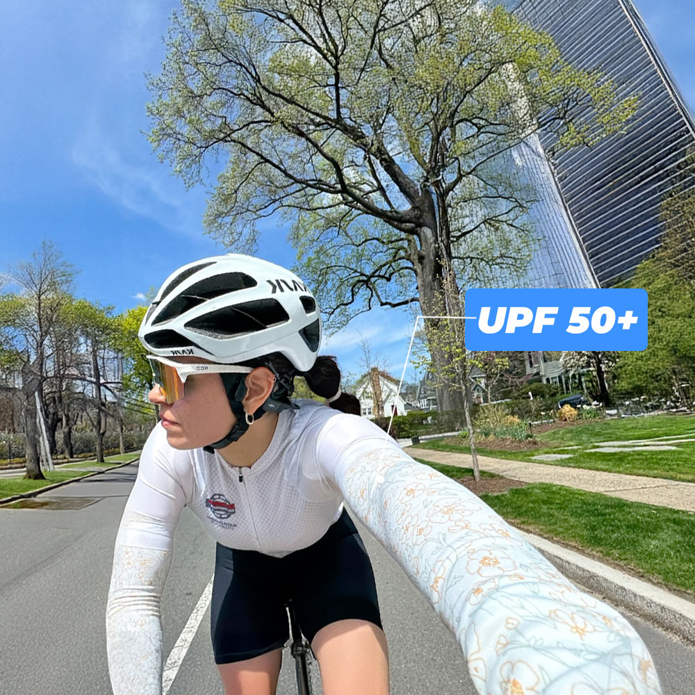 Cyclist wearing a helmet and sunglasses rides on a sunny day with a UPF 50+ label.