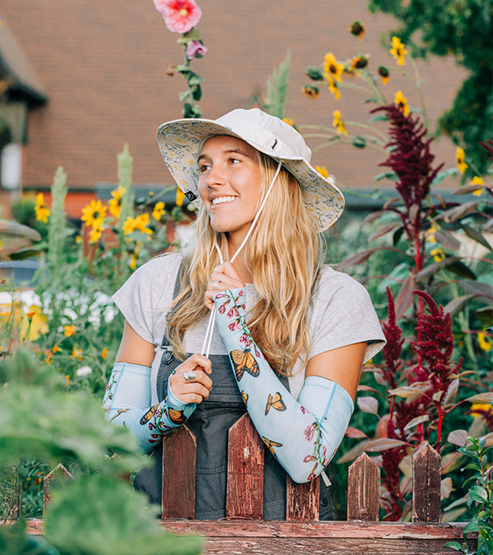 Woman in a garden wearing a sun hat and floral arm sleeves.