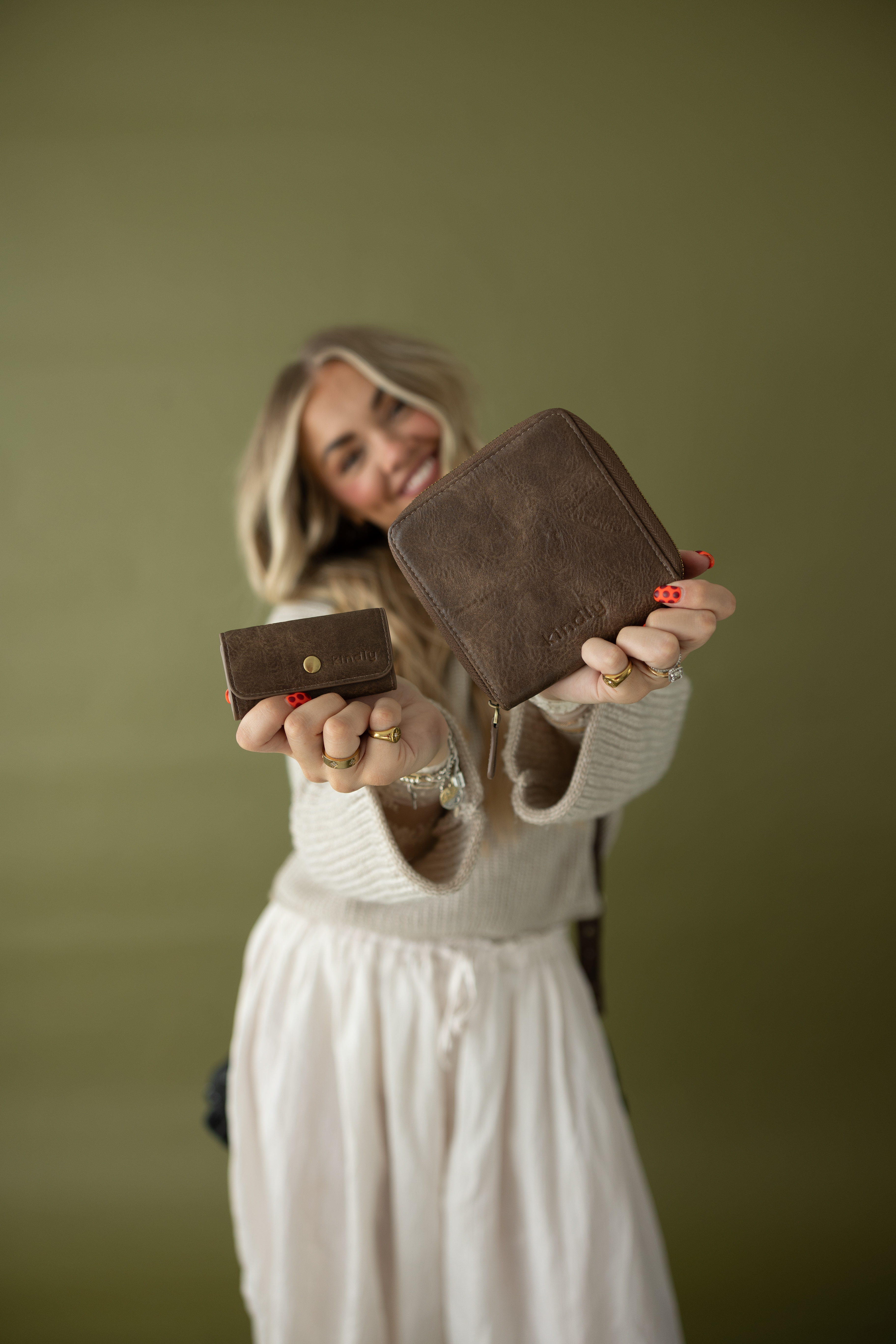 A woman holds up a small brown snap wallet and a larger brown zip-around wallet.