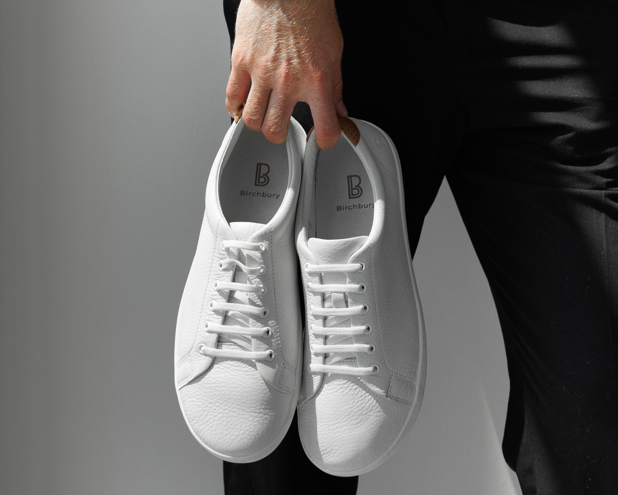 Person holding a pair of white sneakers with 'Birchbury' logo.