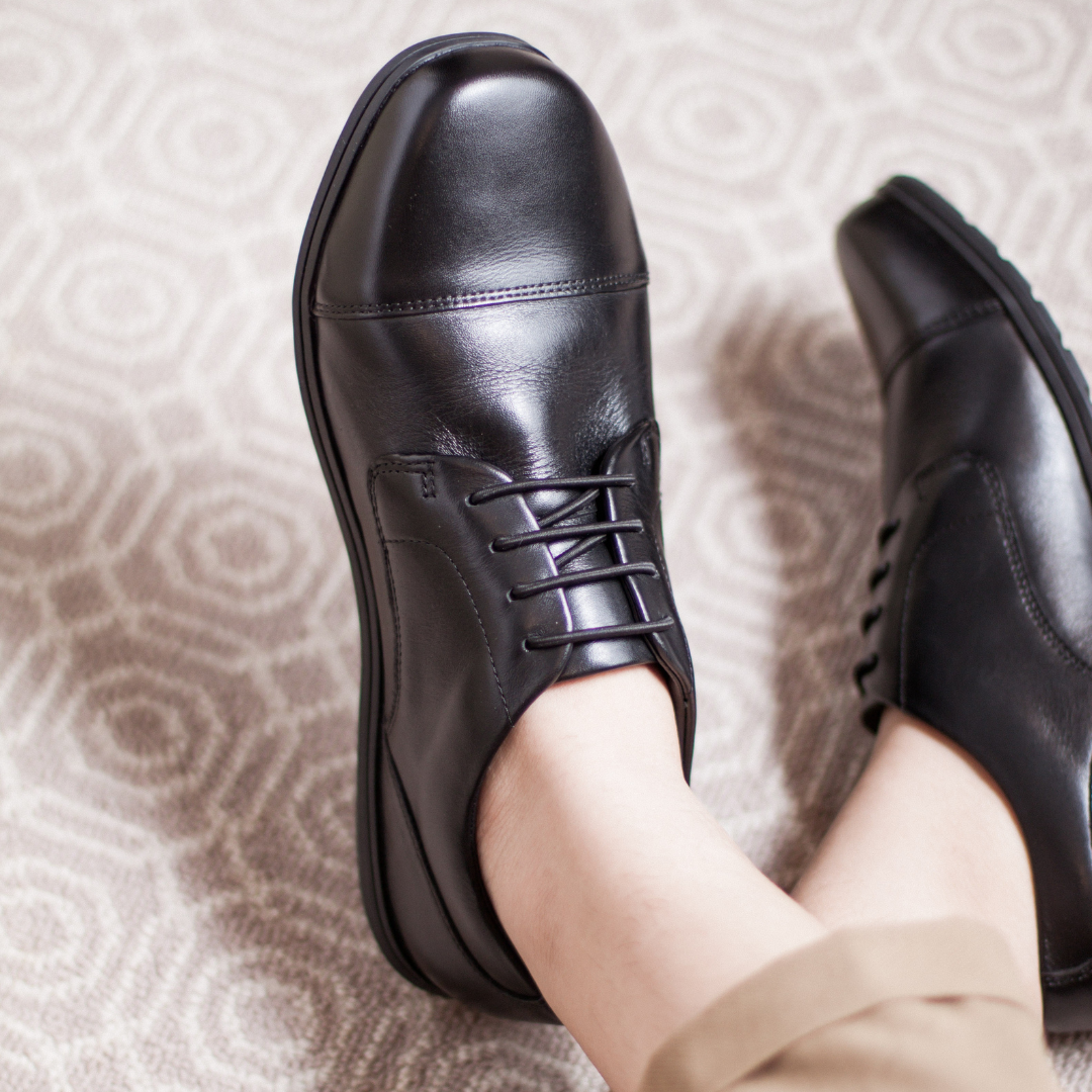 Person wearing black leather shoes on a patterned carpet.