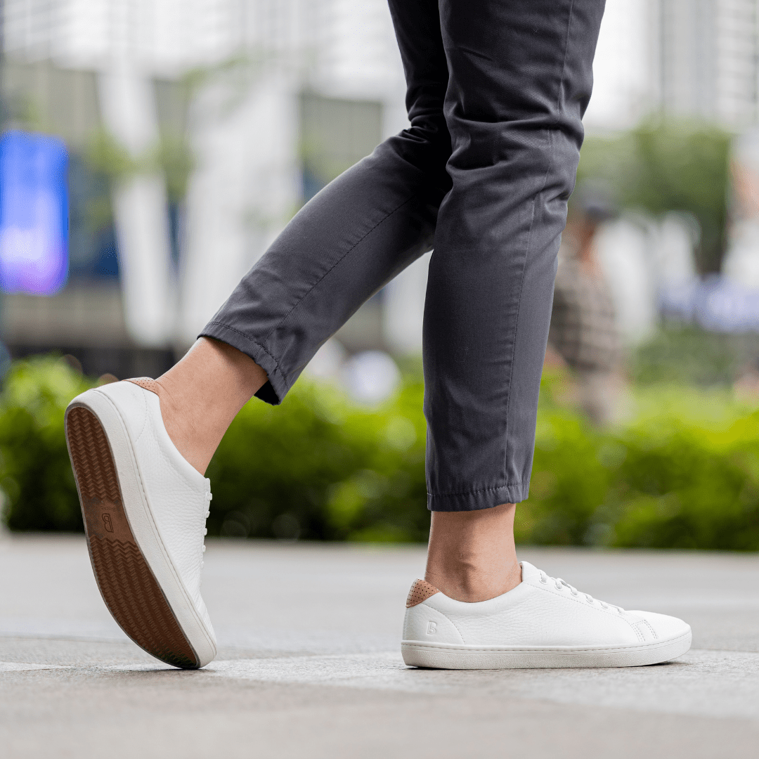 Person wearing white sneakers and gray pants walking outdoors.