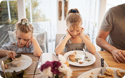 Two children sitting at a dining table with plates of food.