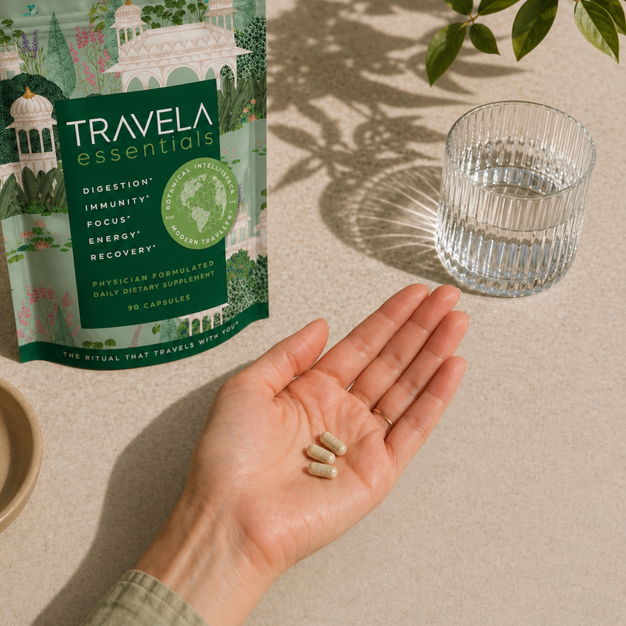 A person holds three capsules in their palm, with a supplement pouch and glass of water nearby.