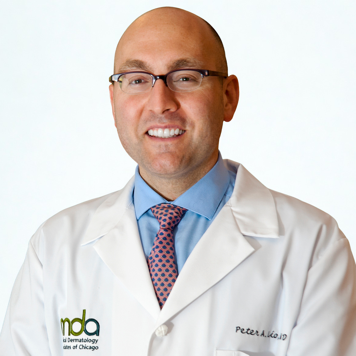 Person in a white lab coat with glasses and a patterned tie, smiling.