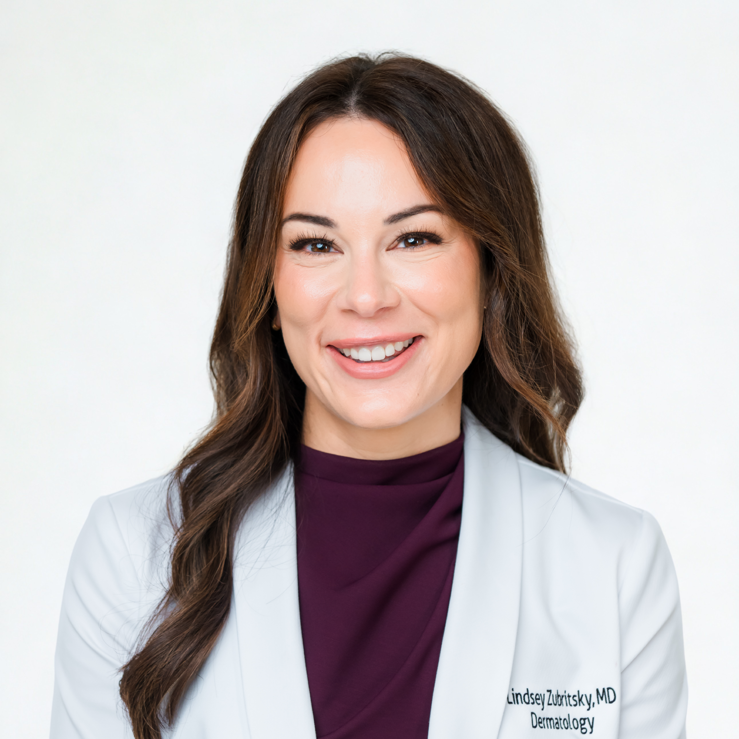 Smiling woman in a white coat with long brown hair.