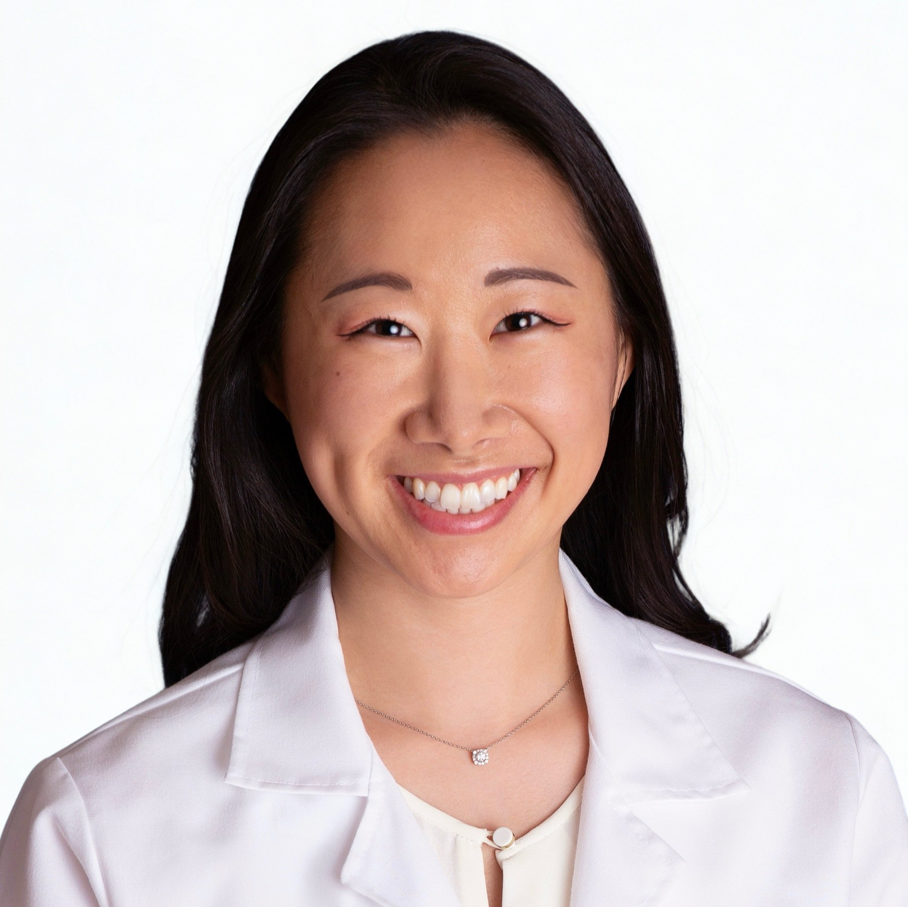 Smiling person wearing a white coat and necklace.