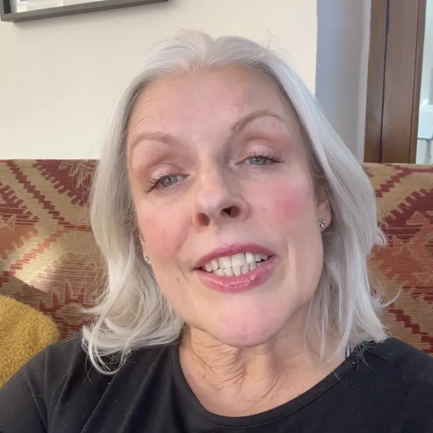 A person with gray hair smiling at the camera indoors.
